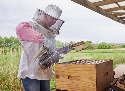 Buy stock photo Shot of a beekeeper using a bee smoker while working on a farm