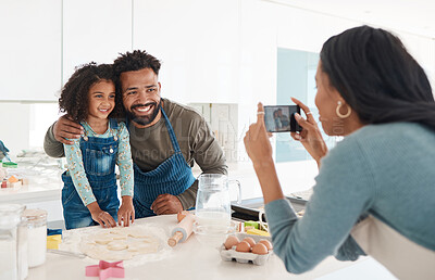 Buy stock photo Cropped shot of an unrecognizable young woman taking a photo of her husband and daughter baking in the kitchen at home