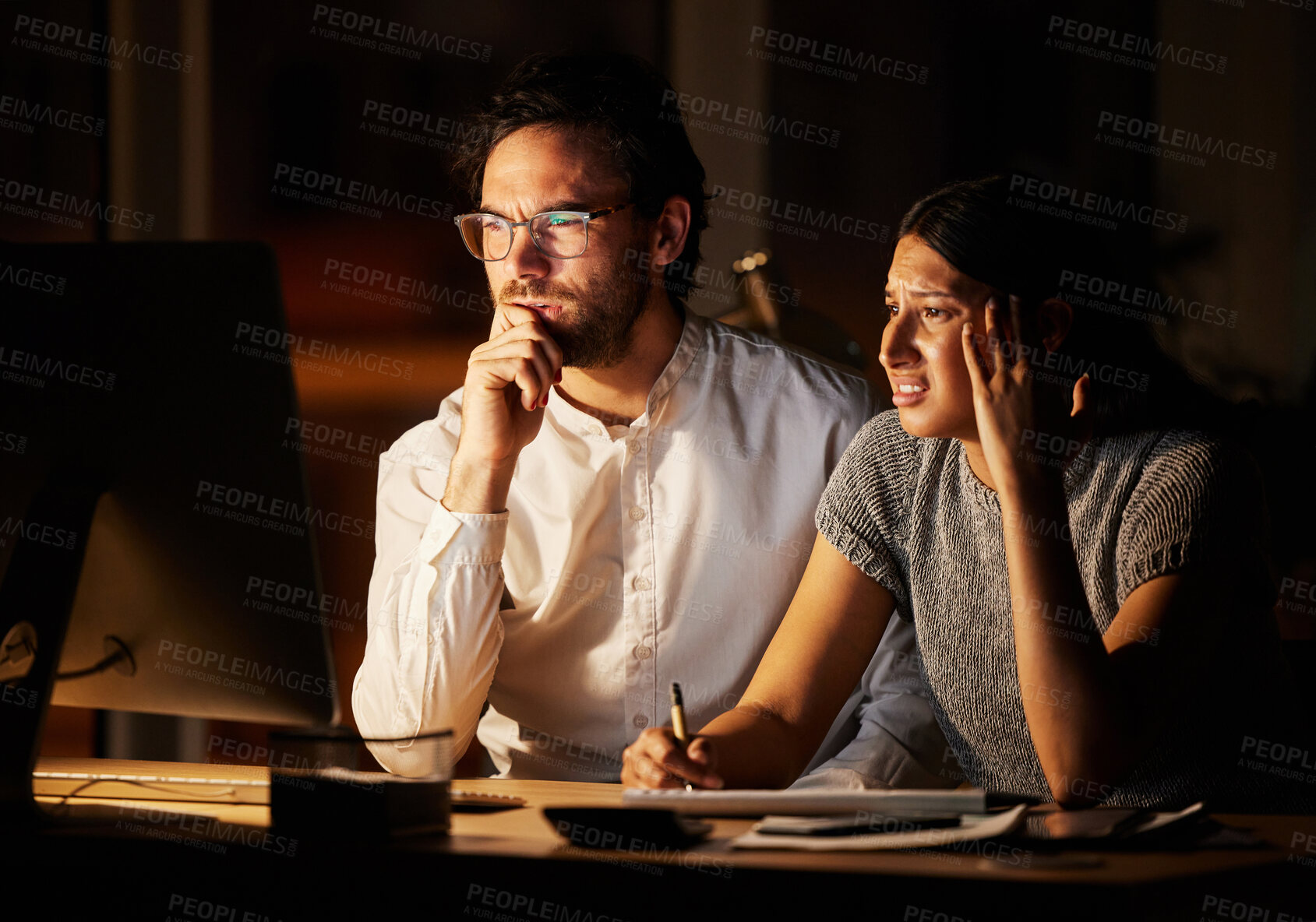 Buy stock photo Shot of two businesspeople looking confused while working together on a computer in an office at night