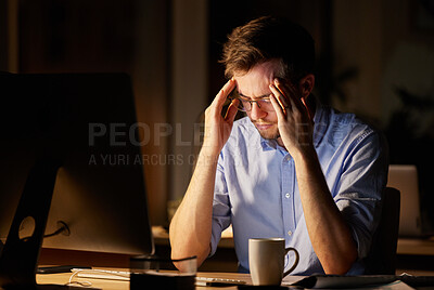 Buy stock photo Shot of a young businessman looking stressed out while working on a computer in an office at night