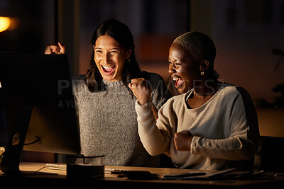 Buy stock photo Shot of two businesswomen cheering while working together on a computer in an office at night