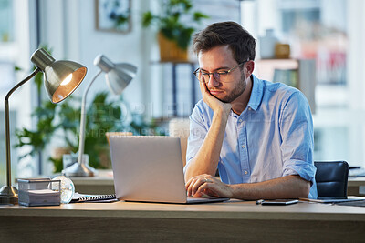 Buy stock photo Shot of a young businessman looking bored while sitting at his desk