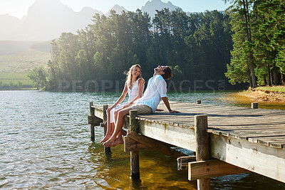 Buy stock photo Young couple, lake and jetty with laughing, happiness and bonding with love in nature for holiday. Man, woman and comic joke on bridge by water to relax with conversation, care and vacation in summer