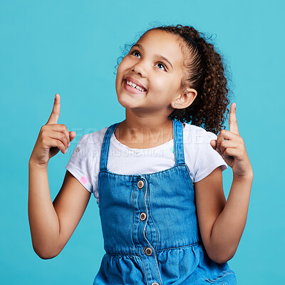 Buy stock photo Happy, looking and a child pointing in a direction isolated on a blue background in a studio. Smile, thinking and a young girl showing up with a hand gesture, advertising and counting on a backdrop