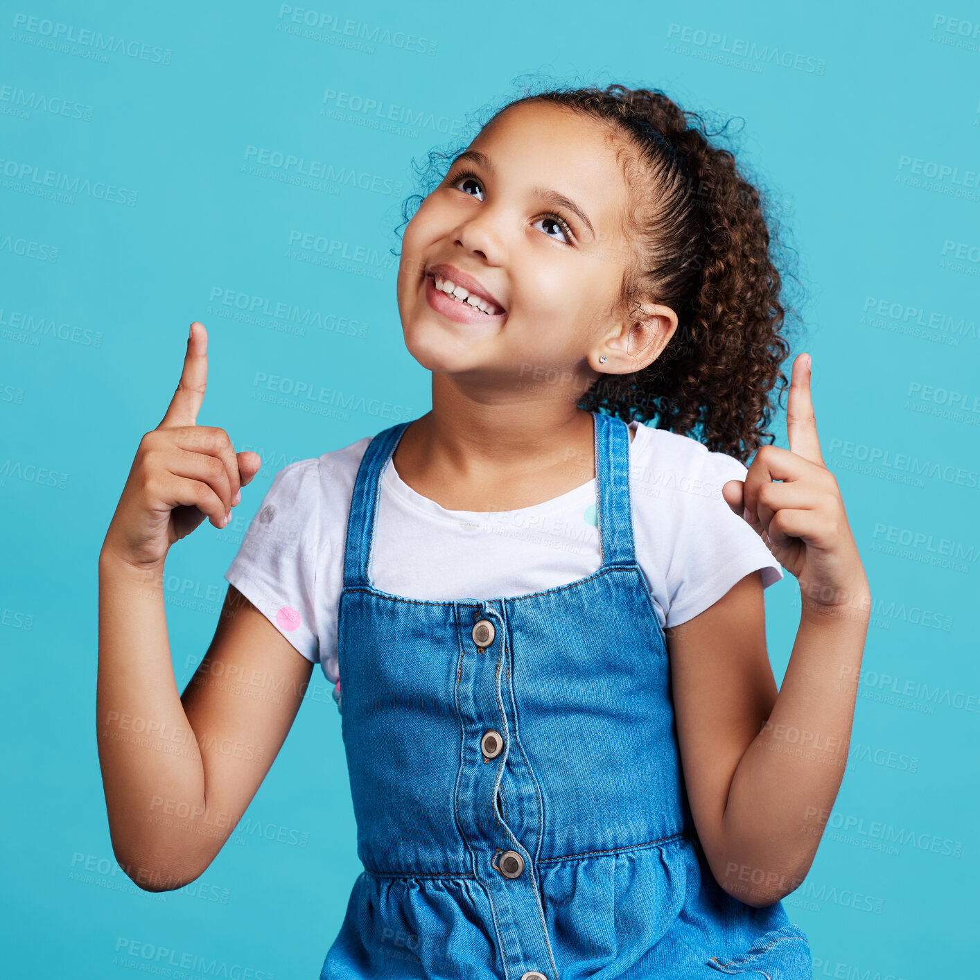 Buy stock photo Happy, looking and a child pointing in a direction isolated on a blue background in a studio. Smile, thinking and a young girl showing up with a hand gesture, advertising and counting on a backdrop