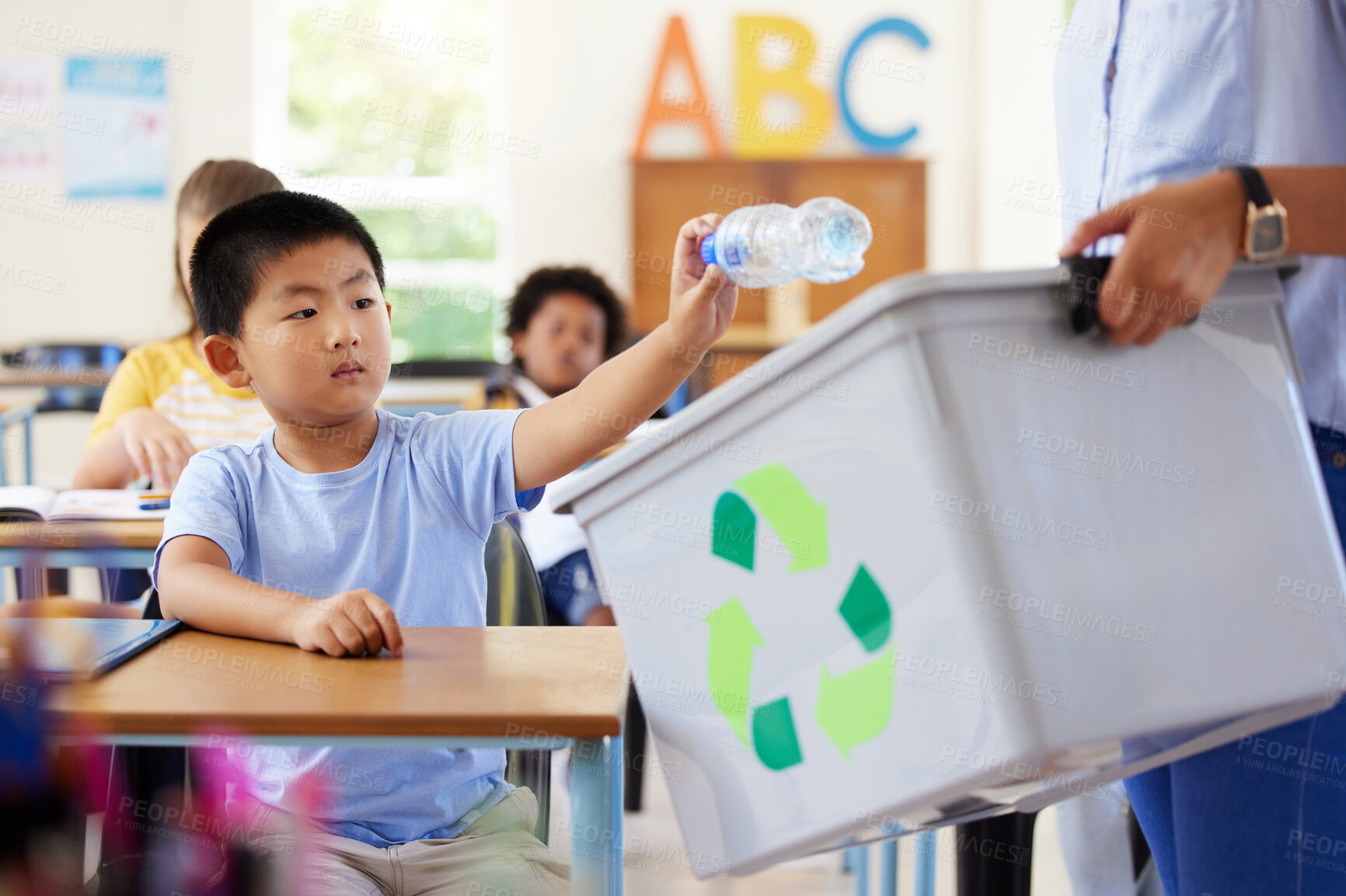 Buy stock photo Teacher, recycle bin and kid in classroom throwing trash for cleaning, climate change or eco friendly in school. Recycling plastic, sustainable learning or education with boy student in kindergarten.