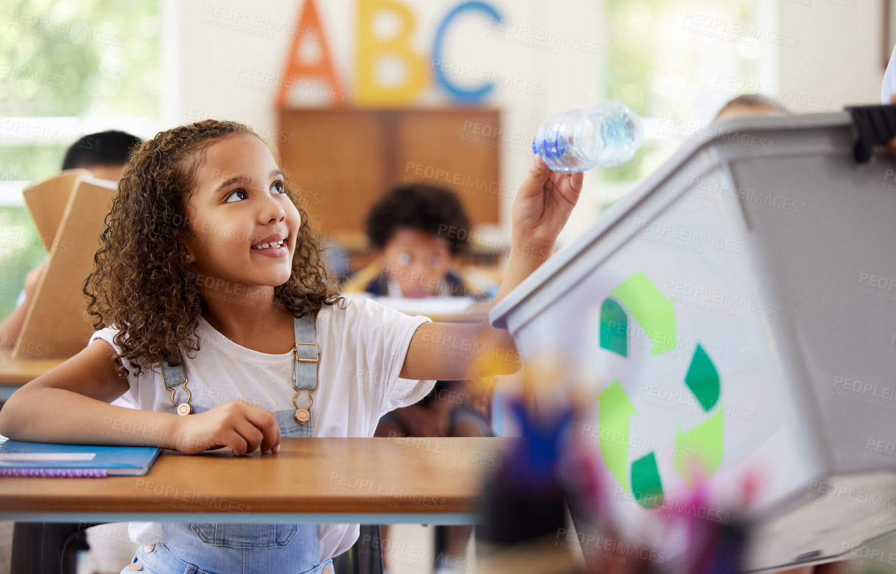 Buy stock photo Learning, recycle bin and girl in classroom throwing trash for cleaning, climate change or eco friendly in school. Recycling plastic, smile and education with happy student or kid in kindergarten.