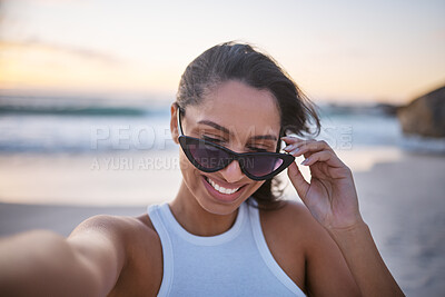 Buy stock photo Shot of a beautiful young woman wearing sunglasses and taking a selfie while at the beach