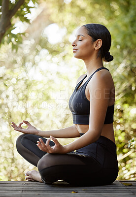 Buy stock photo Full length shot of an attractive young female athlete meditating while practicing yoga outdoors