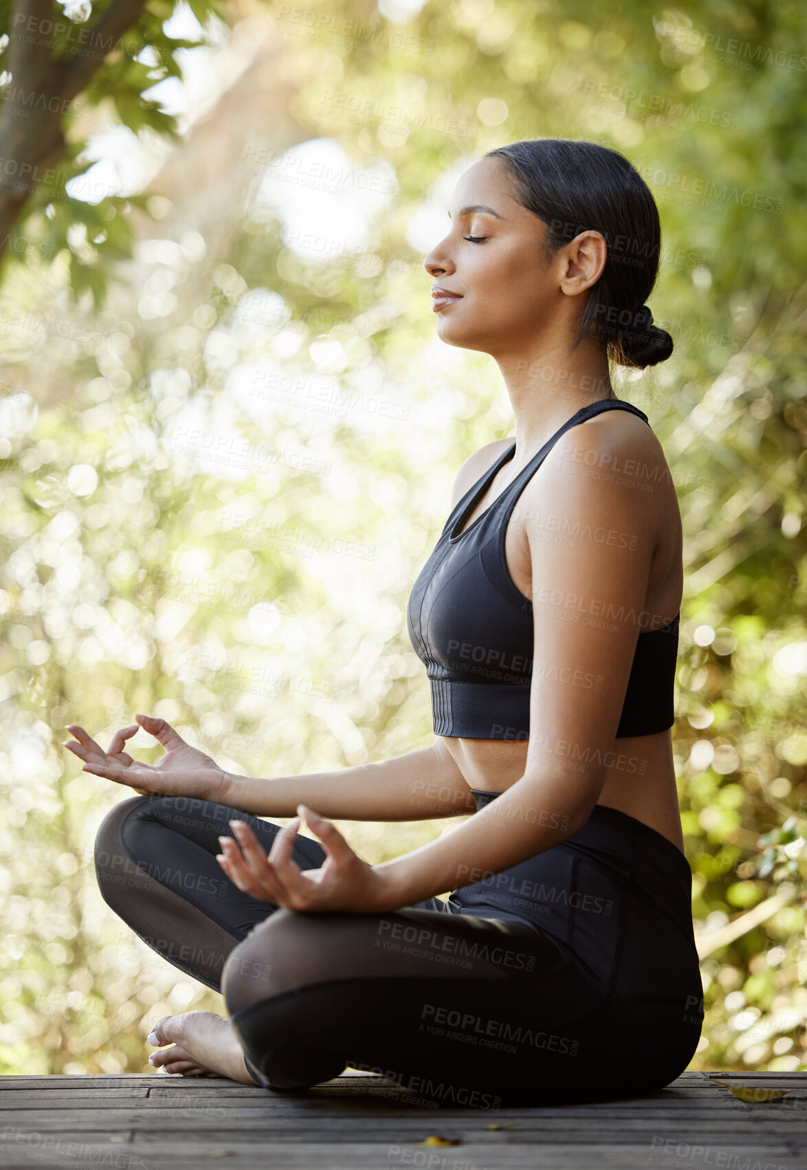 Buy stock photo Full length shot of an attractive young female athlete meditating while practicing yoga outdoors