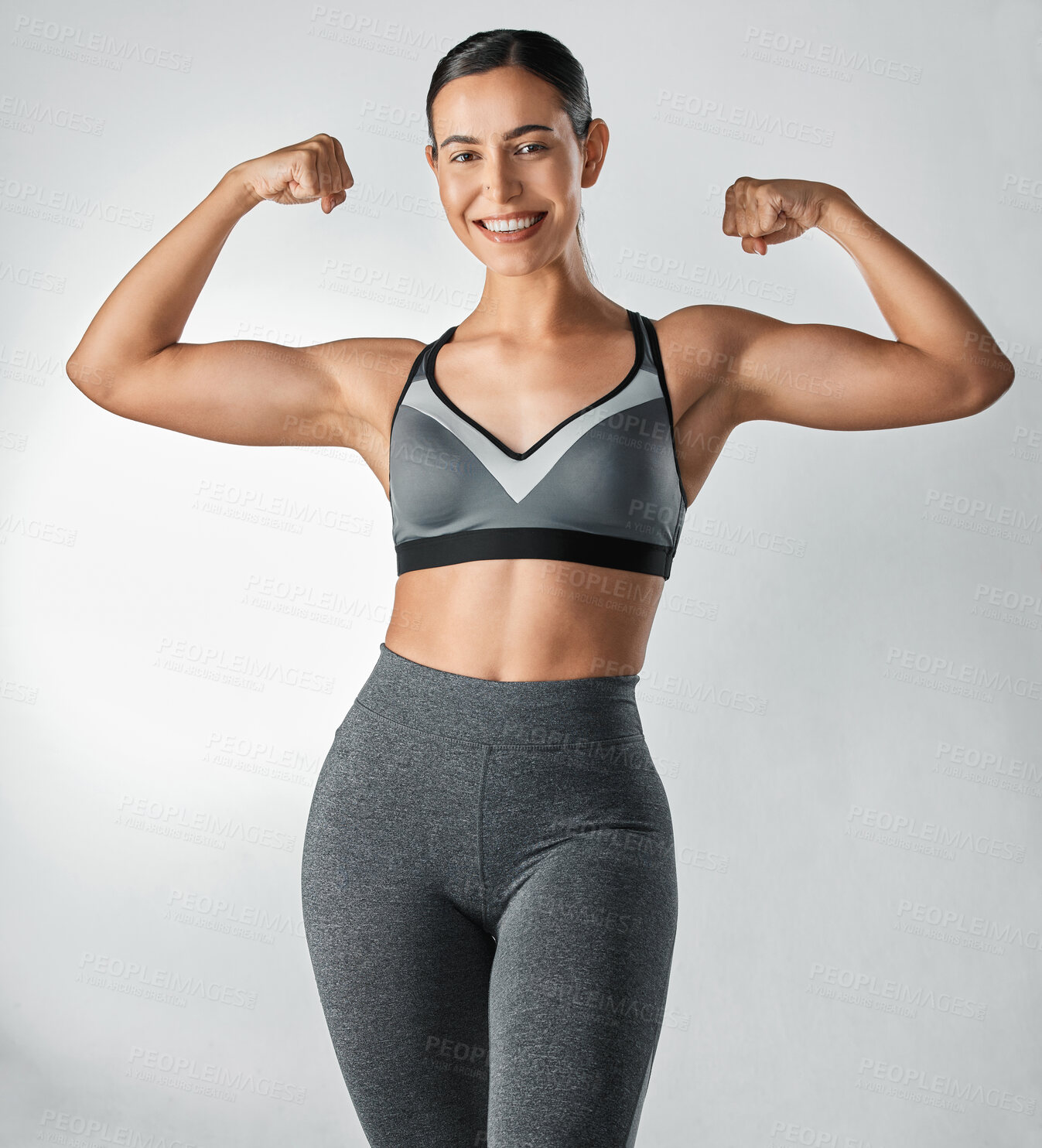 Buy stock photo Studio portrait of a sporty young woman flexing her arms against a grey background