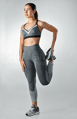 Buy stock photo Studio shot of a sporty young woman stretching her legs against a grey background