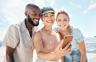 Buy stock photo Shot of a diverse group of friends standing together and using a cellphone to take selfies during a day outdoors