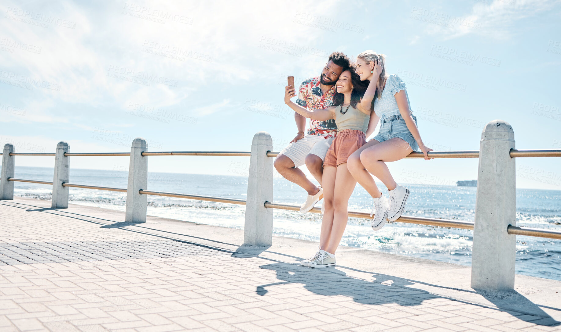 Buy stock photo Full length shot of a diverse group of friends standing together and using a cellphone to take selfies outdoors