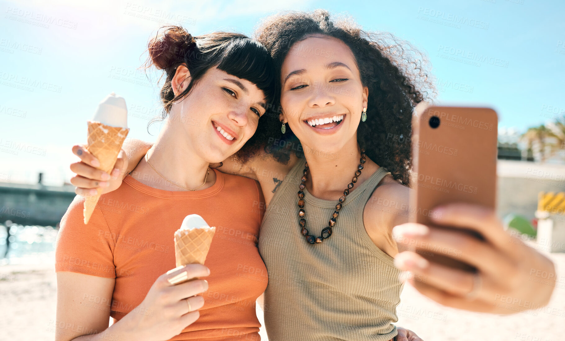 Buy stock photo Cropped shot of two attractive young girlfriends taking selfies while enjoying ice creams on the beach
