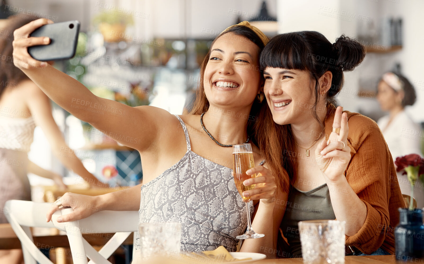 Buy stock photo Shot of two friends taking selfies using a smartphone at a restaurant