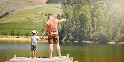 Buy stock photo Back, lake and a father holding hands with his son while looking at the view while outdoor in nature together. Love, family or kids with a man and boy child standing on a pier for bonding by water
