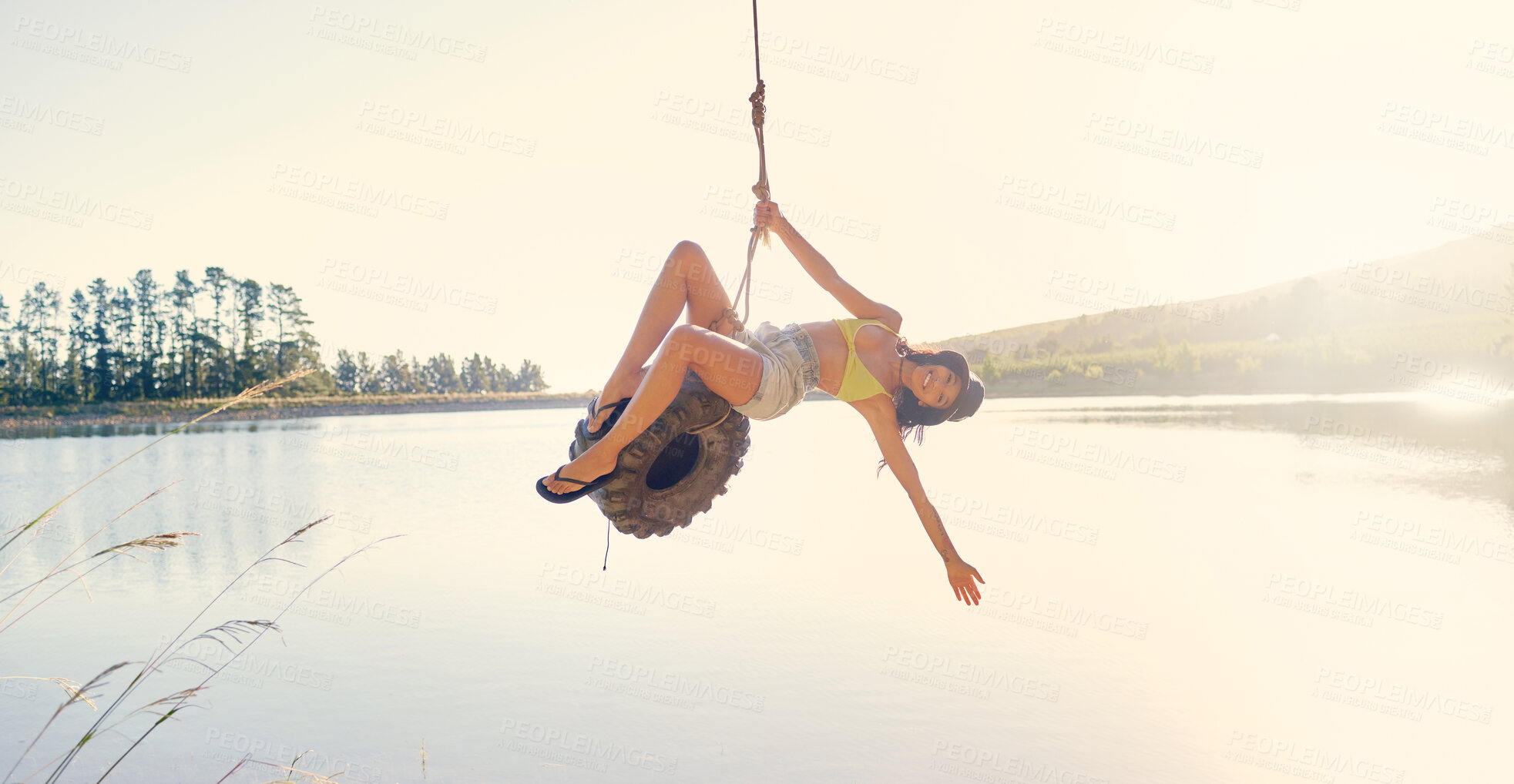 Buy stock photo Lake, rope swing and a woman outdoor in nature sitting on a tyre for carefree fun or adventure during summer. Water, freedom and travel with a young tourist in the wilderness for holiday or vacation