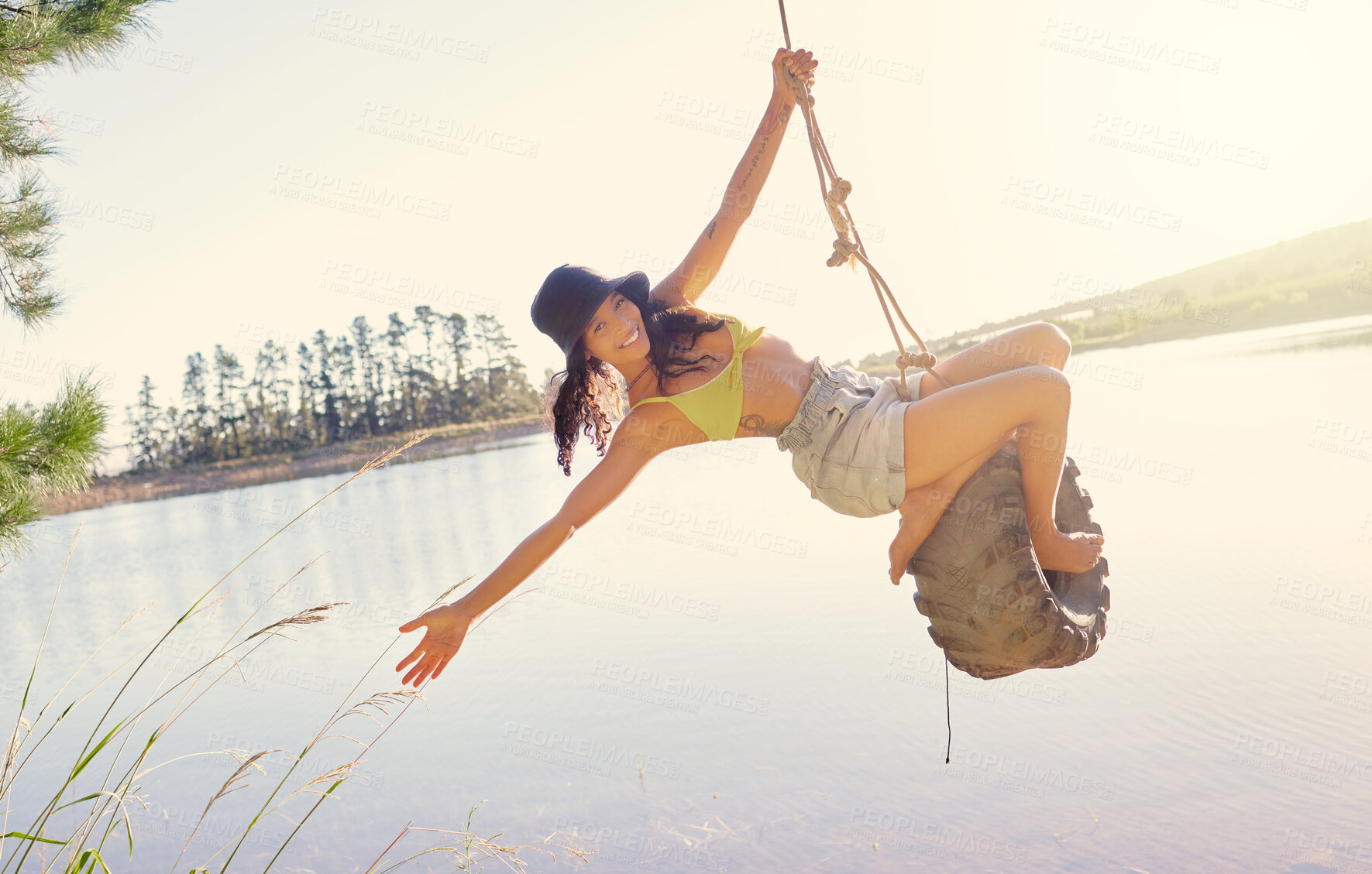 Buy stock photo Lake, rope swing and a woman in nature sitting on a tyre for carefree fun or adventure during summer. Water, freedom and travel with a young tourist outdoor in the wilderness for holiday or vacation