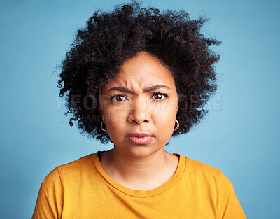 Buy stock photo Portrait, frown and anger with an african woman on a blue background in studio looking mad or serious. Face, bad or negative and an unhappy young female person with an afro feeling frustrated