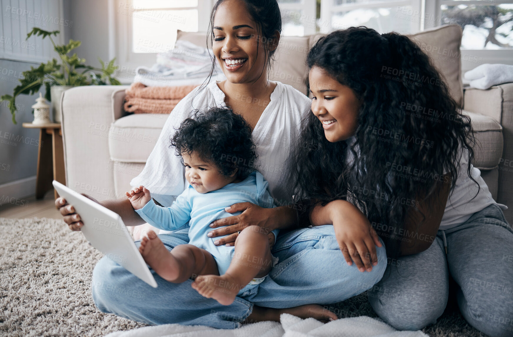 Buy stock photo Full length shot of a young woman sitting in the living room with her children and using a digital tablet