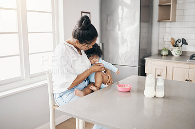 Buy stock photo Shot a young woman sitting in the kitchen with her daughter and feeding her