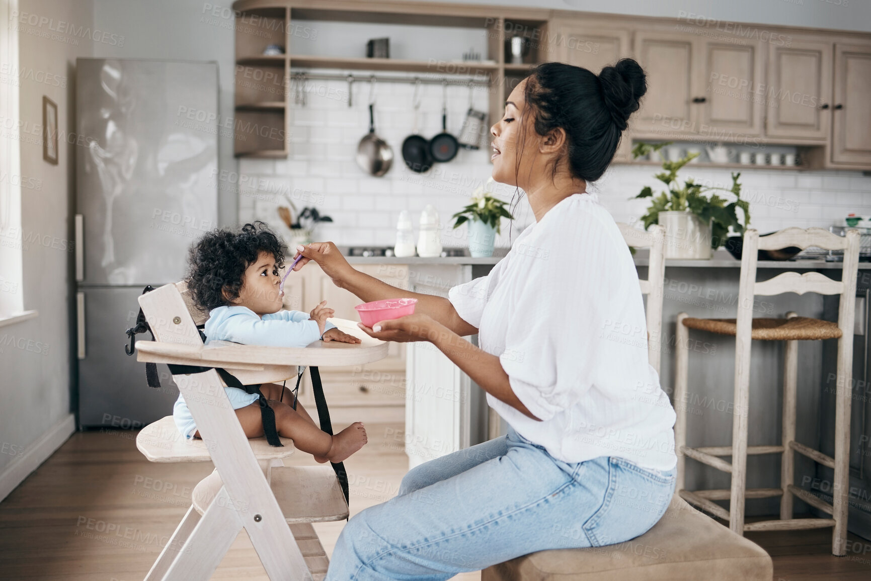 Buy stock photo Shot an attractive young woman sitting in the kitchen with her daughter and feeding her