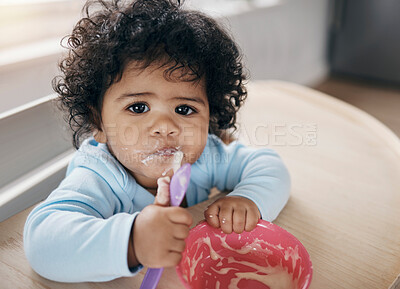 Buy stock photo Shot of an adorable little girl sitting alone in the kitchen and eating her breakfast