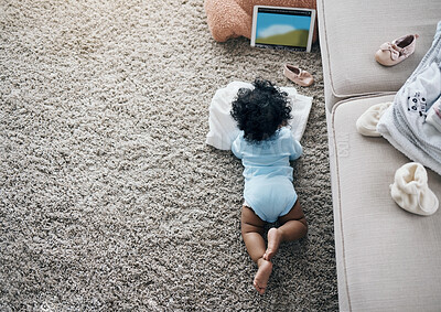 Buy stock photo High angle shot of an unrecognisable baby lying on the living room floor and watching a video on a digital tablet