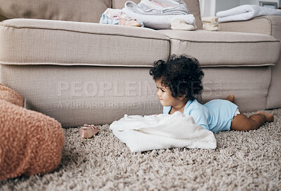 Buy stock photo Full length shot of an adorable little girl lying on the living room floor at home and playing with the laundry