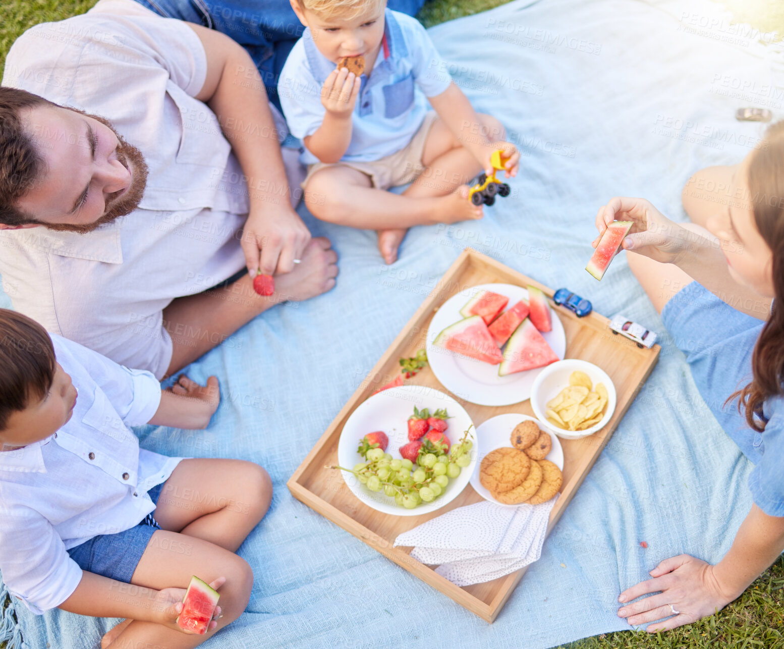 Buy stock photo Family, fruit and picnic in park with above for bonding, nutrition and healthy diet on blanket in nature. Parents, children and eating snack on grass in summer for lunch, holiday and fun activity