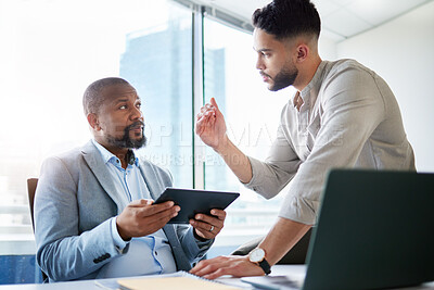 Buy stock photo Shot of two businessmen sitting in the office together and having a discussion while using a digital tablet