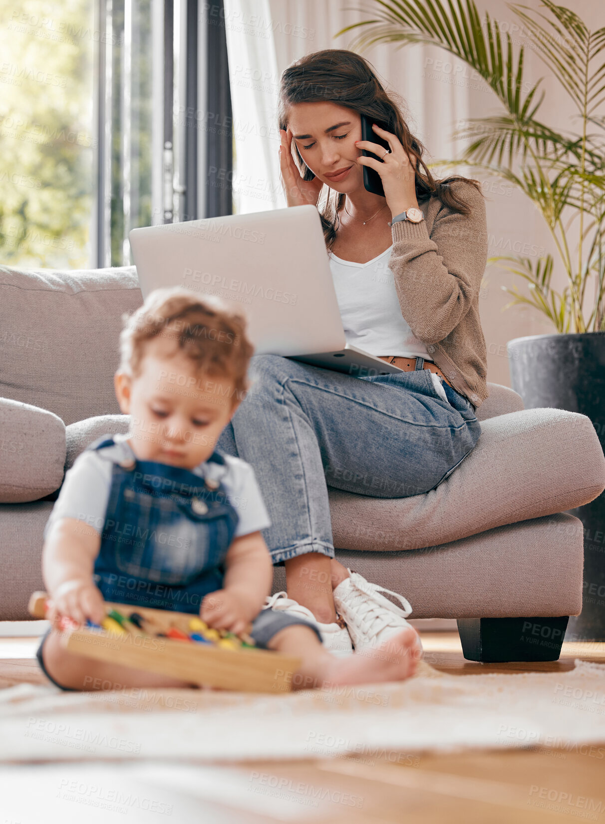 Buy stock photo Shot of a mother using a laptop while her son plays at home