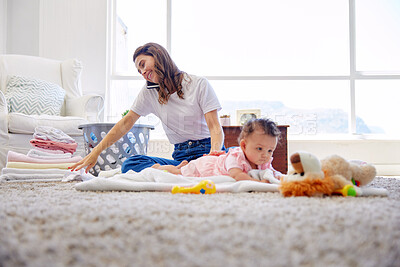 Buy stock photo Shot of a mother folding clothes while her baby plays in the lounge