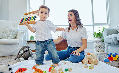 Buy stock photo Full length shot of an adorable little boy playing with his toys at home under the watchful eye of his mother
