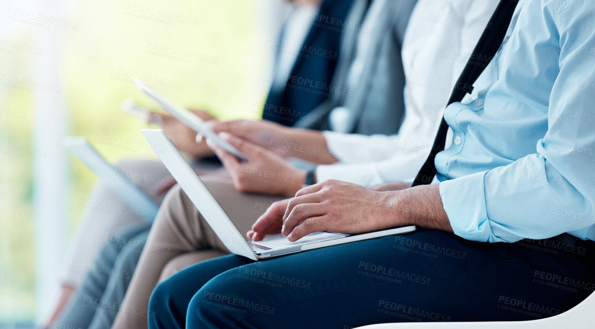 Buy stock photo Shot of an unrecognizable businessman sitting and using his laptop while waiting for an interview in the office