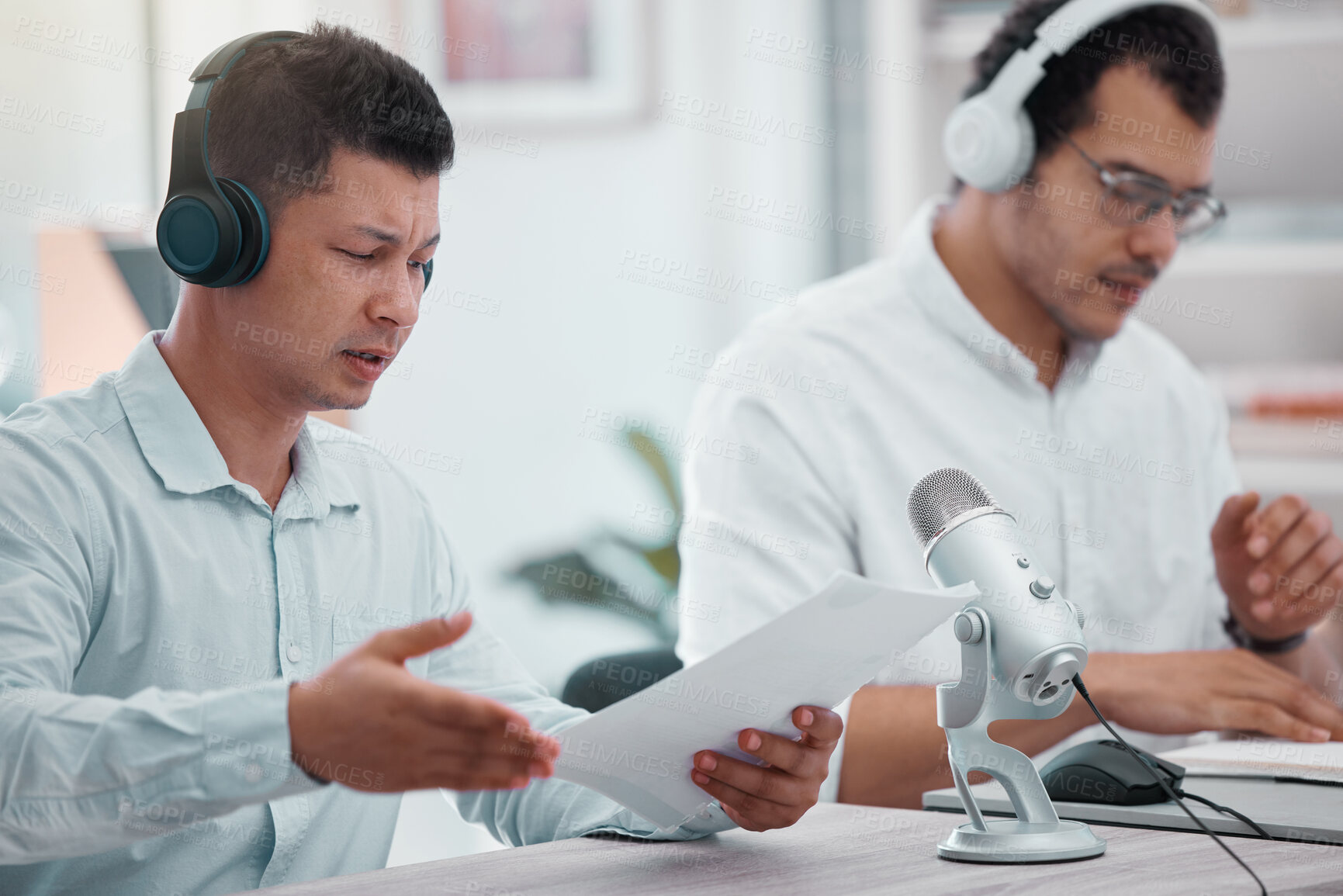 Buy stock photo Shot of two young men going through paper while doing a broadcast in an office