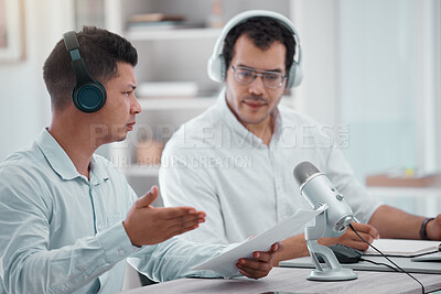 Buy stock photo Shot of two young men going through paper while doing a broadcast in an office