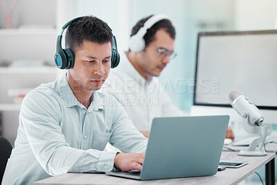 Buy stock photo Shot of a young businessman using a laptop while doing a broadcast in an office with a colleague in the background