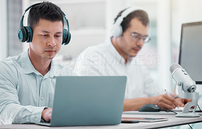 Buy stock photo Shot of a young businessman using a laptop while doing a broadcast in an office with a colleague in the background