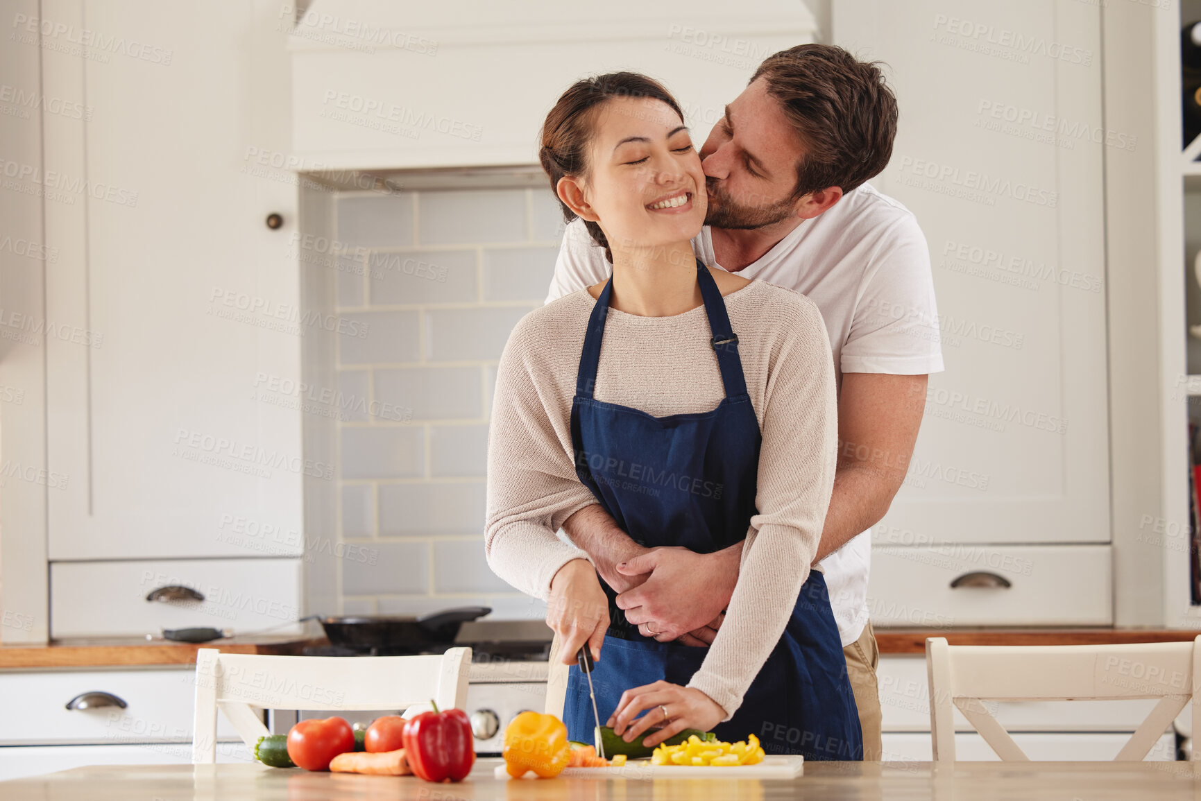 Buy stock photo Happy woman, man and cooking in embrace with kiss in kitchen at home for dinner as partner. Married people, hug and preparing salad for healthy food, diet or nutrition in house or apartment as couple