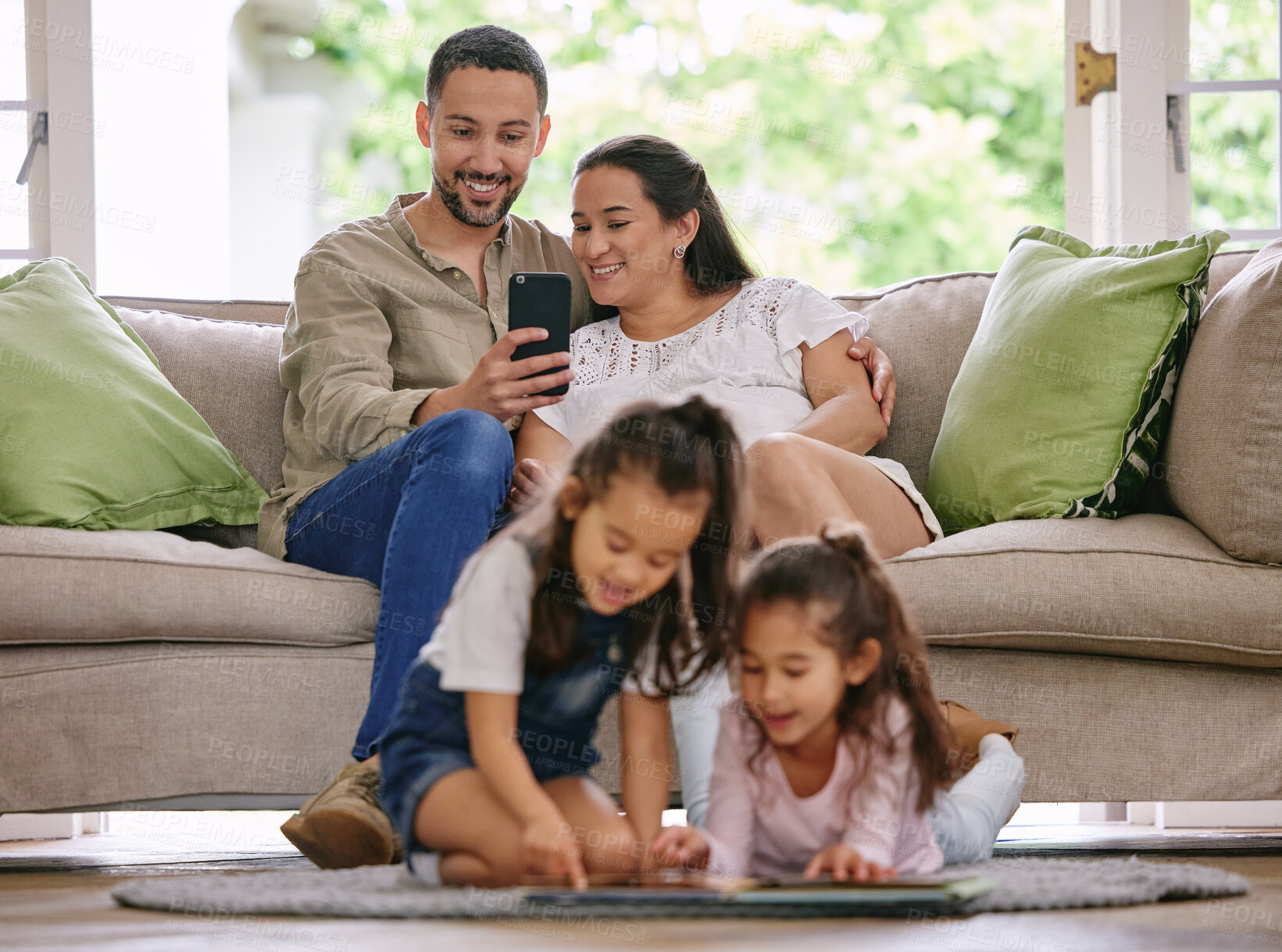 Buy stock photo Family, relax and parents with a phone on a sofa, happy and photo of children reading a book in the living room. Love, bonding and kids learning in their home while relaxing with mother and father