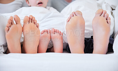 Buy stock photo Shot of an unrecognizable family laying barefoot on a bed at home
