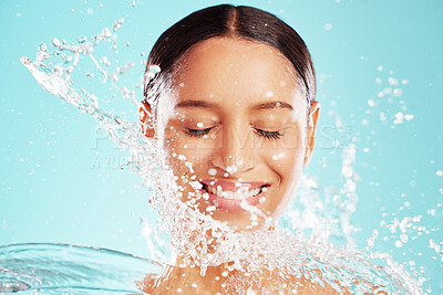 Buy stock photo Cleaning, smile and water splash with face of woman in studio isolated on blue background for hygiene. Beauty, skincare and wellness with happy model at spa for cosmetics, dermatology or hydration