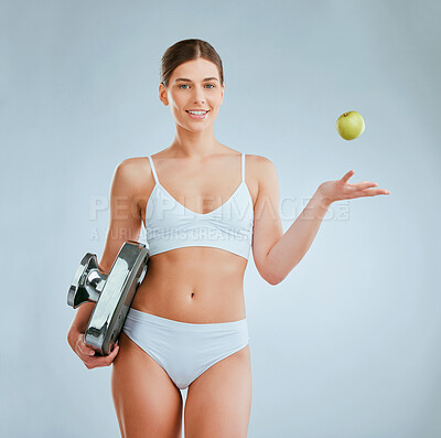 Buy stock photo Studio shot of a young woman posing with an apple and weight scale