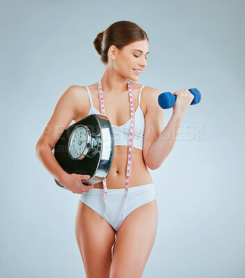 Buy stock photo Studio shot of a young woman posing with a dumbbell and weight scale