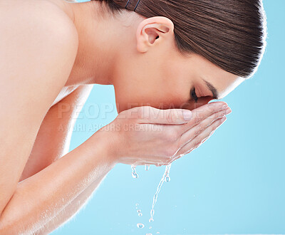 Buy stock photo Woman, water and washing face with liquid for hygiene, hydration or hydro cleanse in studio on a blue background. Young female person or model with mineral or natural aqua for skin cleaning routine