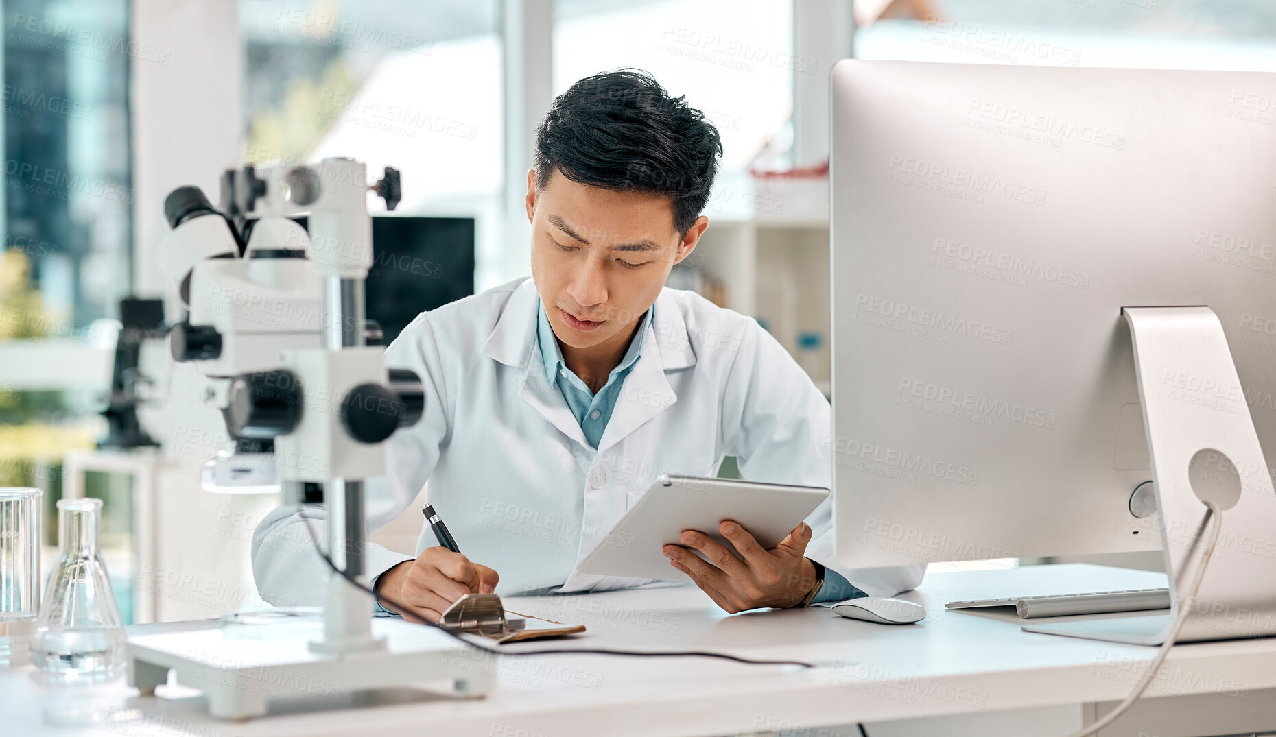 Buy stock photo Shot of a young scientist using a digital tablet and writing notes while working in a lab