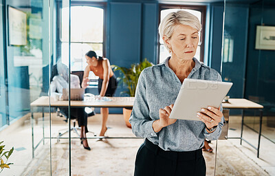 Buy stock photo Cropped shot of an attractive mature businesswoman using a tablet while standing in an office doorway