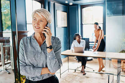 Buy stock photo Cropped shot of an attractive mature businesswoman making a phonecall while standing in an office doorway